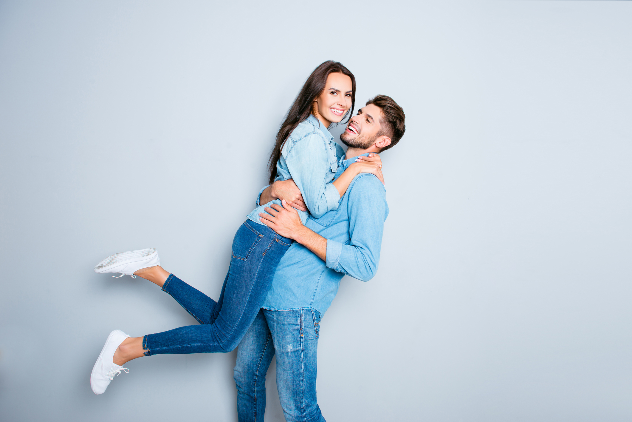 Happy man carrying his pretty wife on gray background