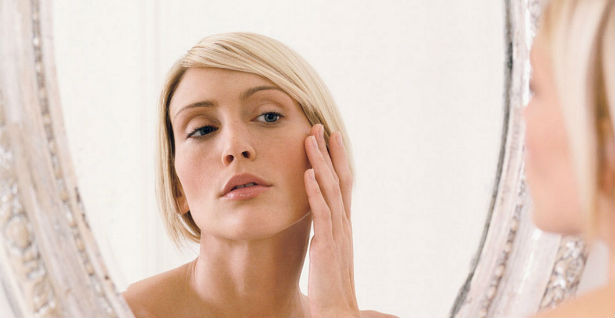 Young-woman-looking-in-mirror-hand-to-face